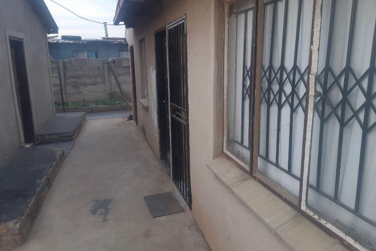 A narrow exterior side passage featuring concrete paving, security gates on doors and windows, and a perimeter boundary wall.