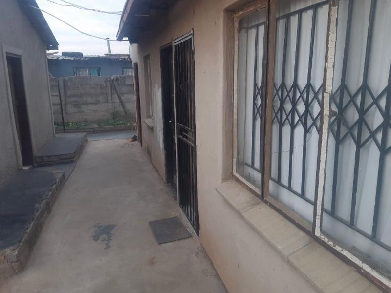 A narrow exterior side passage featuring concrete paving, security gates on doors and windows, and a perimeter boundary wall.