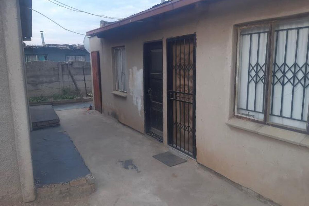 Rear exterior view of the property featuring concrete paving, security gates on doors and windows, and a corrugated metal roof.