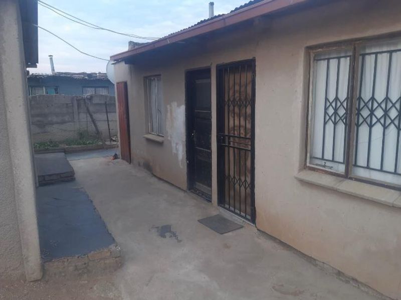 Rear exterior view of the property featuring concrete paving, security gates on doors and windows, and a corrugated metal roof.
