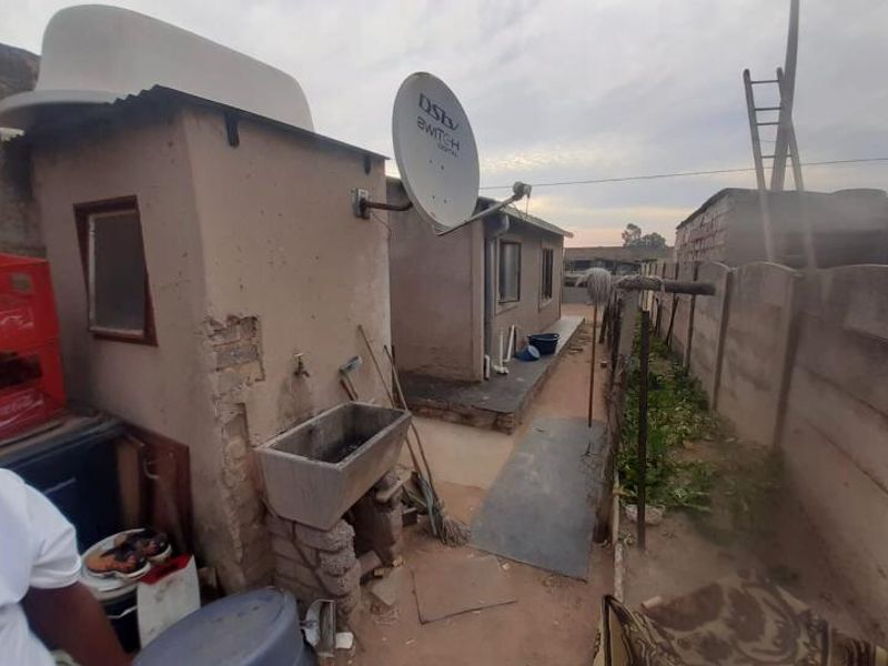 Rear exterior view showing a utility area with a concrete sink, satellite dish, and precast boundary walling in need of maintenance.