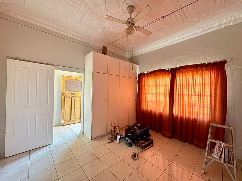 A bedroom featuring a classic pressed metal ceiling, built-in cupboards, and tiled flooring, requiring cosmetic updates to restore its character.