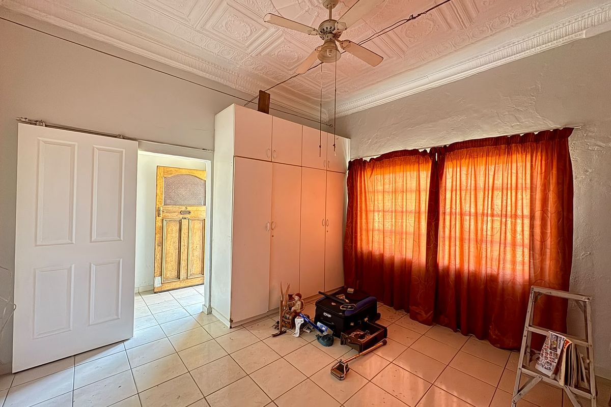 A bedroom featuring a classic pressed metal ceiling, built-in cupboards, and tiled flooring, requiring cosmetic updates to restore its character.