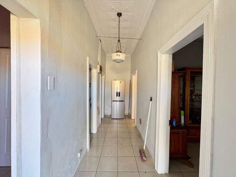 A long hallway featuring tiled flooring, a decorative pressed metal ceiling, and a vintage pendant light fixture, connecting multiple rooms.