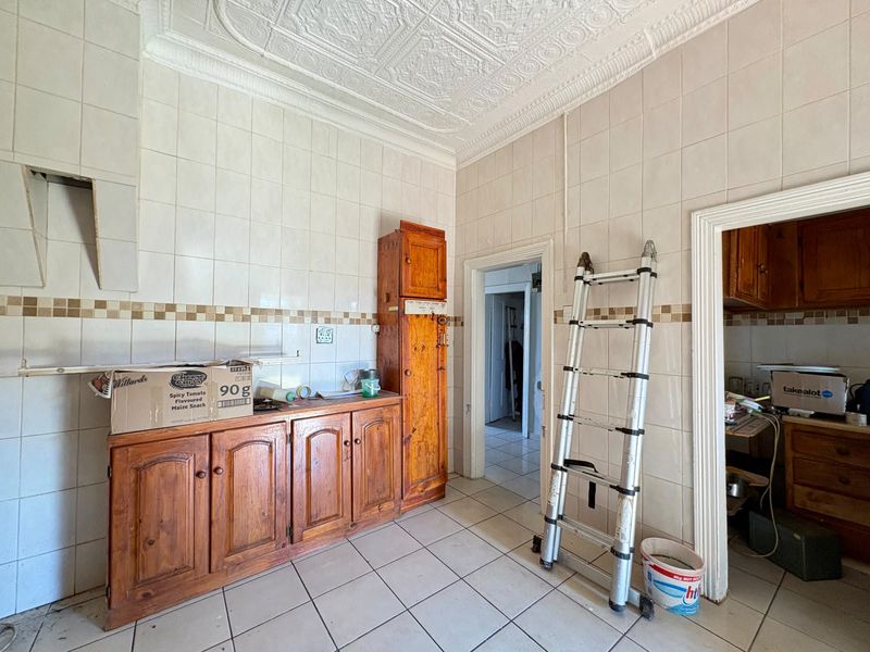 A dated kitchen featuring wooden cabinetry, tiled walls, and a decorative pressed metal ceiling, requiring renovation to modernize the space.