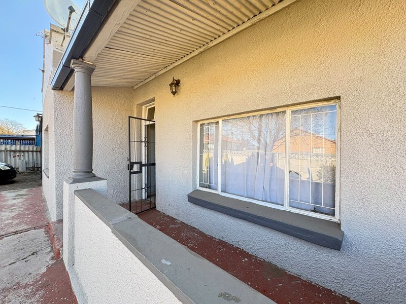 A covered front patio area featuring a security gate, security bars on the window, and a concrete column support.