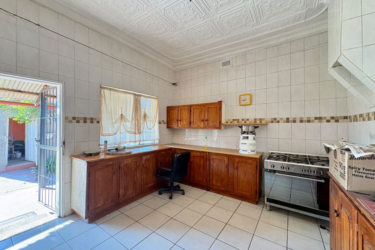 A dated kitchen featuring wooden cabinetry, tiled walls, and a gas stove, with direct access to an outdoor area through a security gate.