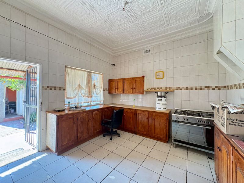 A dated kitchen featuring wooden cabinetry, tiled walls, and a gas stove, with direct access to an outdoor area through a security gate.