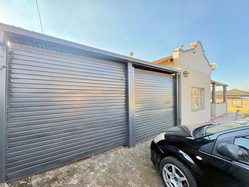 A double garage featuring dark metal roller doors and a cobblestone driveway, set against a textured exterior wall with a gabled roof detail.