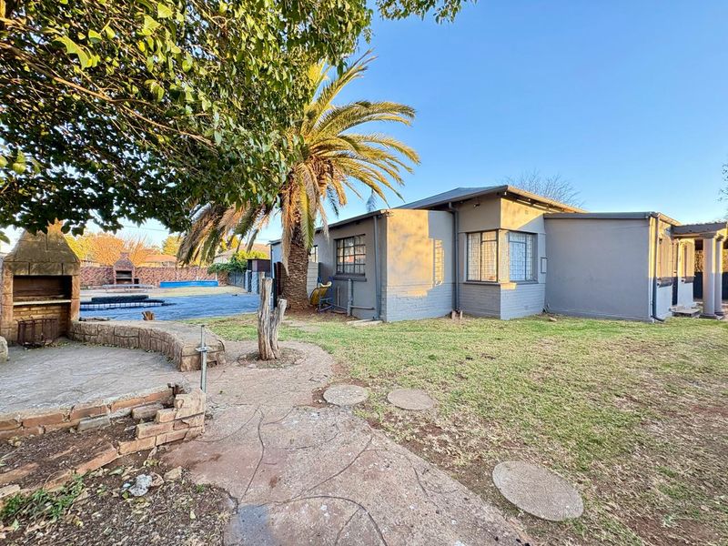 Rear exterior view featuring a built-in braai, paved patio area, swimming pool, and established garden space.