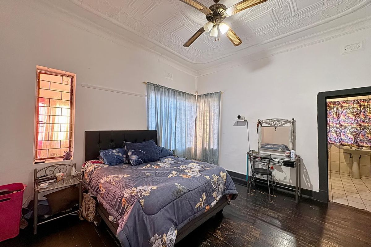 Spacious bedroom featuring original decorative pressed metal ceilings, timber flooring, and a ceiling fan, with an adjoining ensuite bathroom.