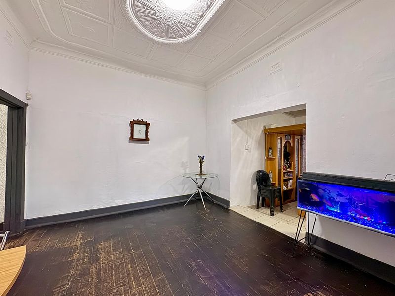 Living room featuring original pressed metal ceilings with ornate rose and dark timber flooring, offering a character-filled space ready for renovation.