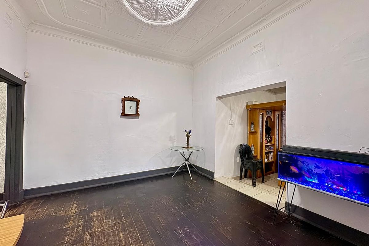 Living room featuring original pressed metal ceilings with ornate rose and dark timber flooring, offering a character-filled space ready for renovation.