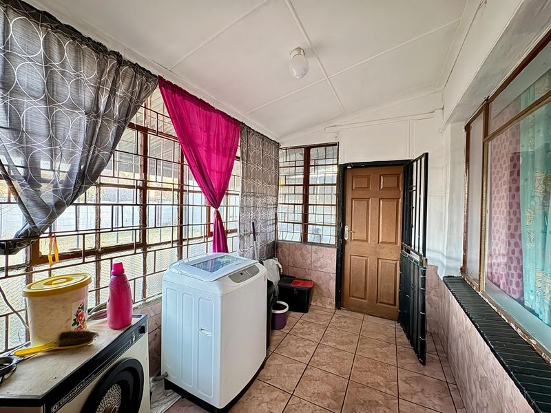 A functional laundry area featuring tiled flooring, wall cladding, and secure window bars, providing a practical utility space with direct exterior access.
