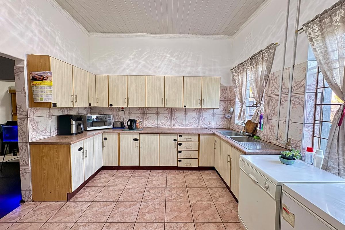 A functional kitchen featuring laminate cabinetry, double bowl stainless steel sink, ceramic wall and floor tiles, and a tongue and groove ceiling.