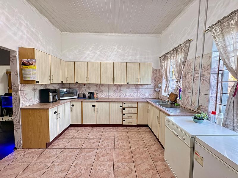 A functional kitchen featuring laminate cabinetry, double bowl stainless steel sink, ceramic wall and floor tiles, and a tongue and groove ceiling.