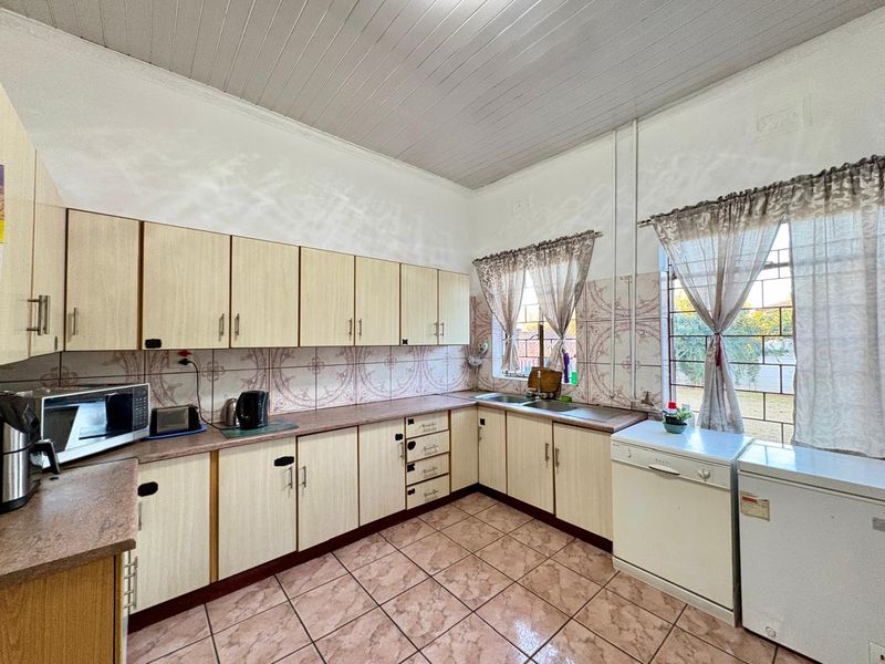A functional kitchen featuring laminate cabinetry, patterned wall tiles, and ceramic flooring, offering a practical layout with ample storage and workspace.