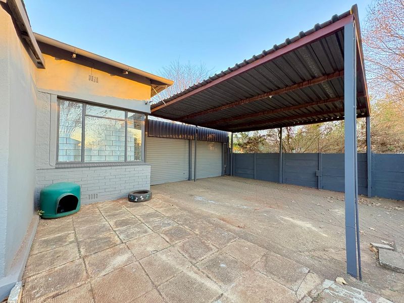 Exterior view of a paved driveway area featuring a covered carport and secure metal garage doors.