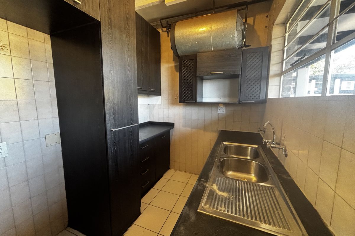 A compact kitchen featuring dark built-in cabinetry, a double stainless steel sink, and tiled finishes, currently vacant and ready for modernization.