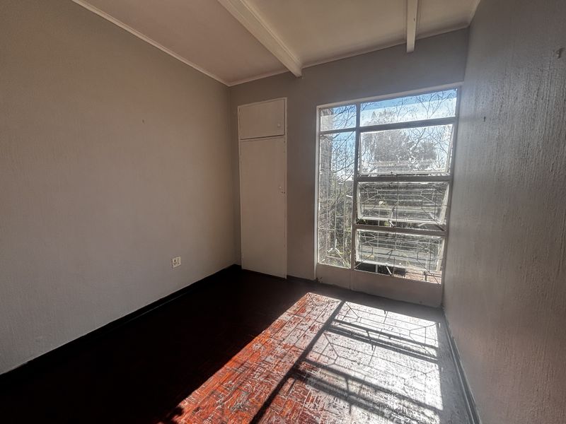 An empty bedroom featuring original parquet flooring, a built-in cupboard, and a large steel-framed window with security bars.