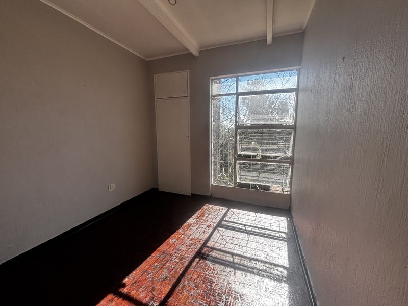 An empty bedroom featuring original parquet flooring, a built-in cupboard, and a large steel-framed window allowing for natural light.
