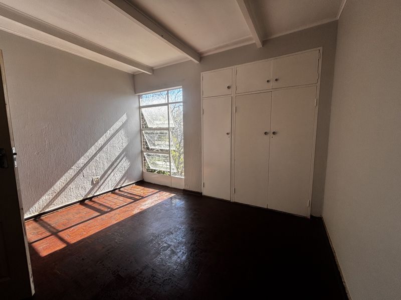 A bright, empty bedroom featuring original wooden flooring, built-in storage cupboards, and louvered windows that allow for natural light.
