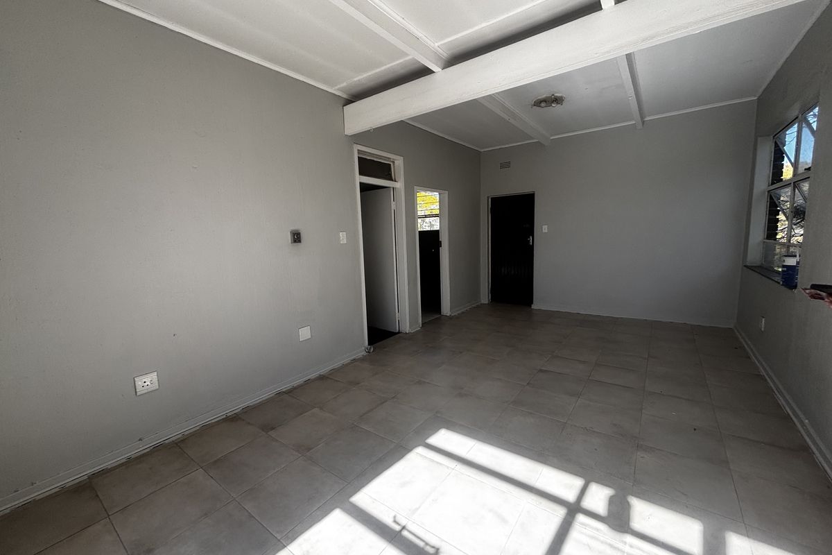 An empty, neutrally painted living area featuring tiled flooring and exposed ceiling beams, offering a blank canvas for interior design.