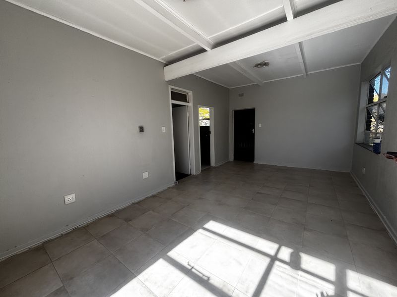 An empty, neutrally painted living area featuring tiled flooring and exposed ceiling beams, offering a blank canvas for interior design.