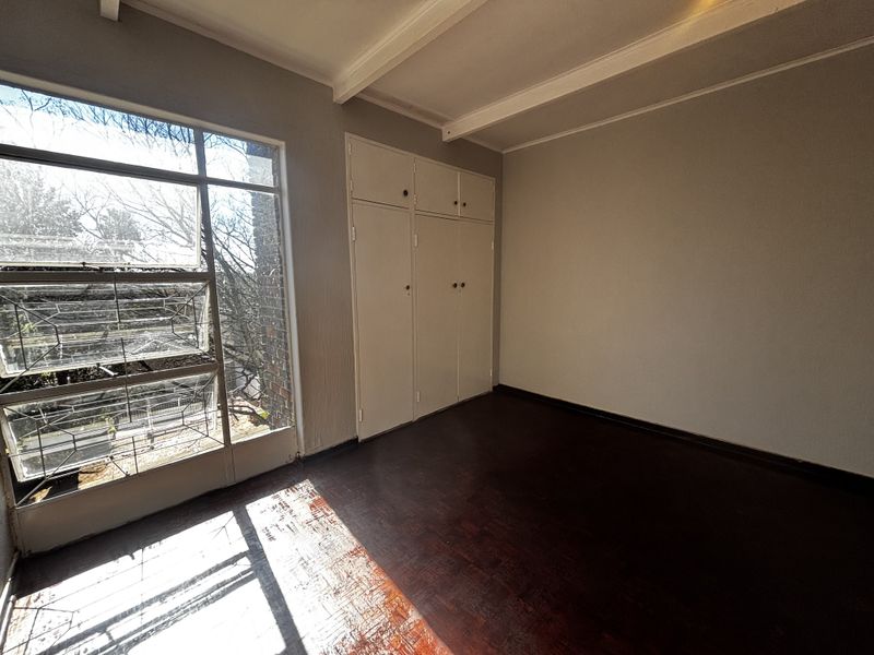 An empty bedroom featuring original parquet flooring, built-in cupboards, and a large window providing natural light.