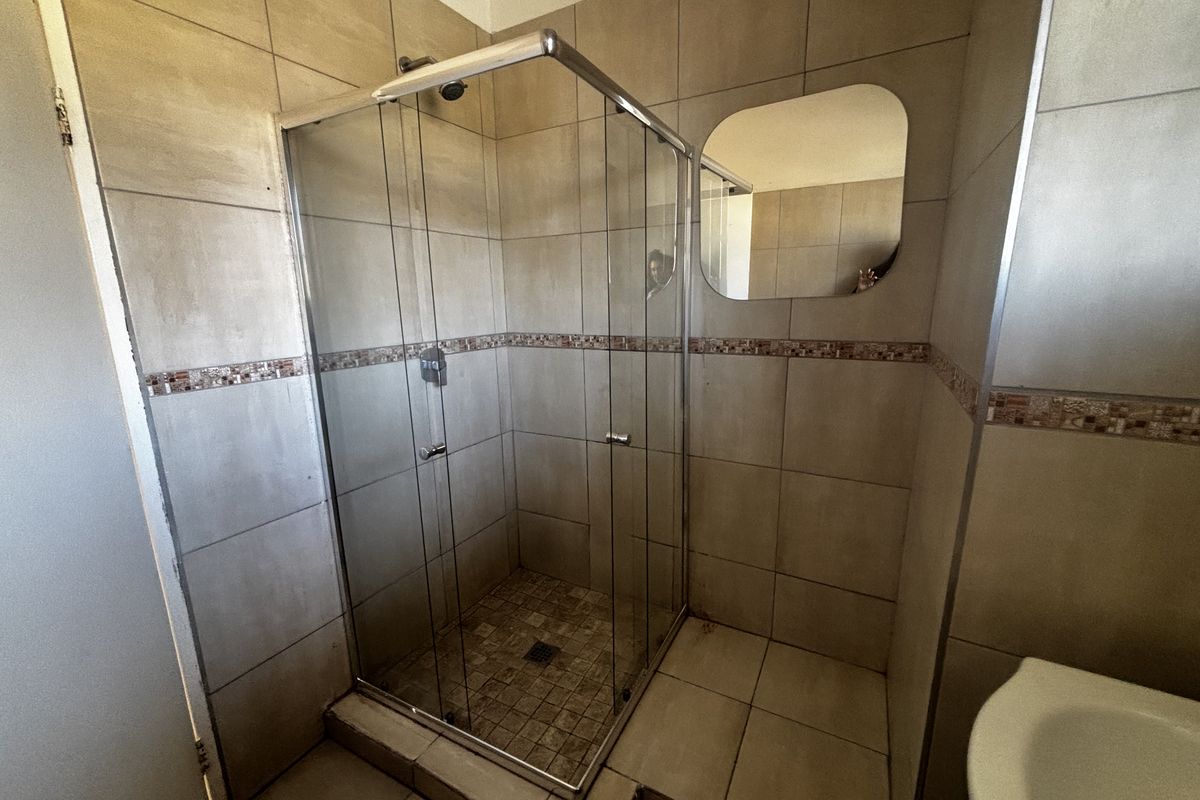A functional bathroom featuring a glass-enclosed shower, neutral ceramic wall and floor tiles, and a wall-mounted mirror.