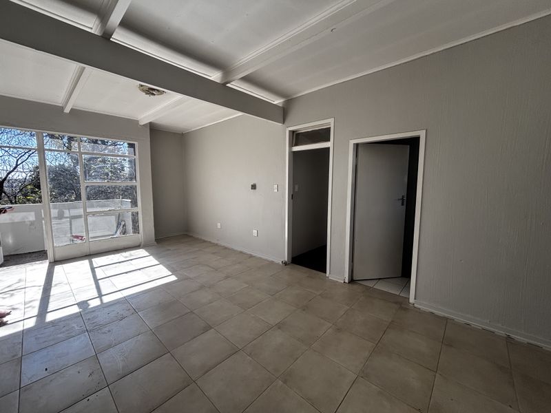 An empty living room featuring tiled flooring, exposed beam ceilings, and a large glass door providing access to an outdoor balcony area.