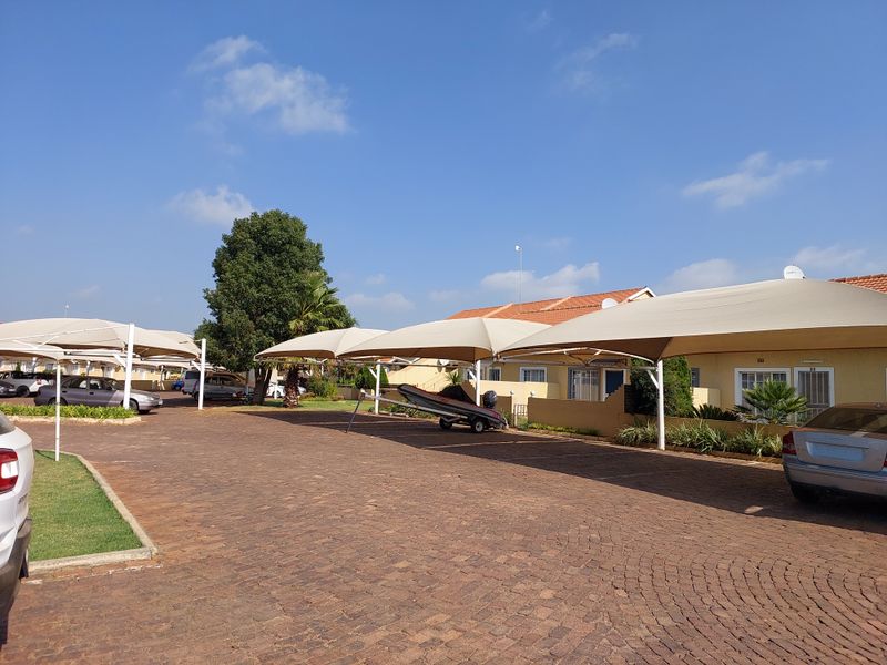 Exterior view of a townhouse complex featuring paved driveway access and multiple covered parking bays with shade cloth structures.