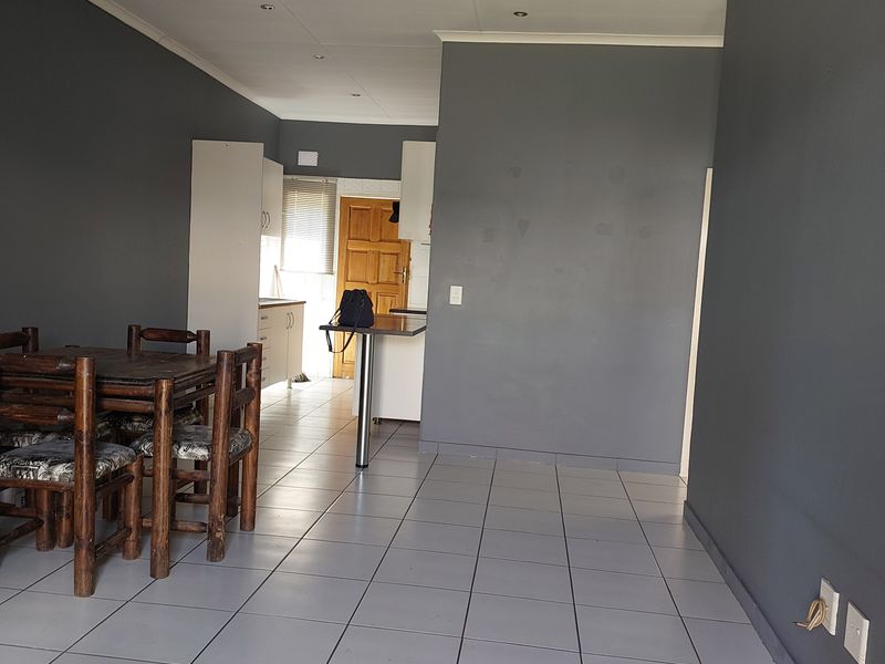 Open plan living and dining area featuring grey walls, tiled flooring, and a functional kitchen space with a breakfast bar.