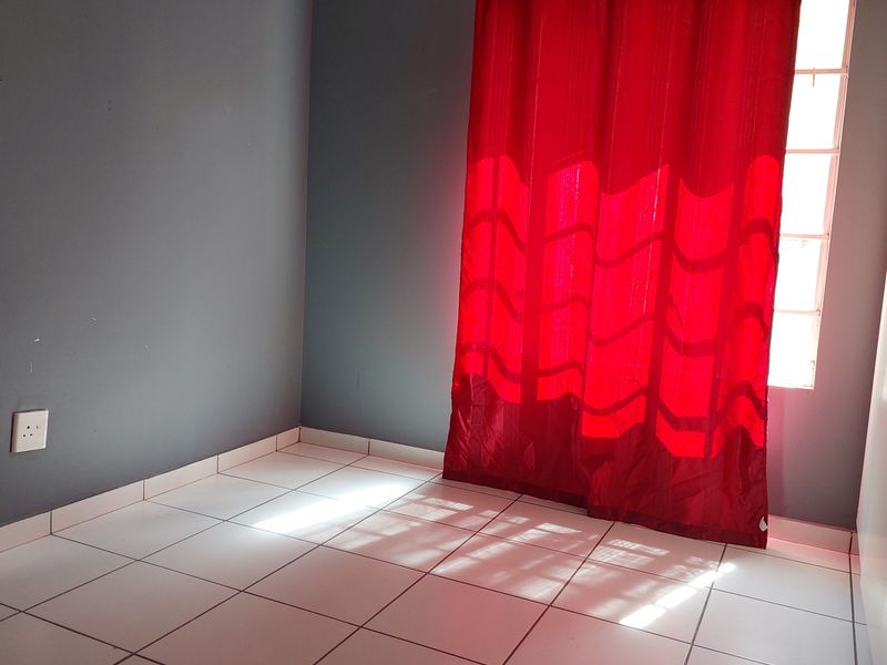 An empty bedroom featuring tiled flooring, a window with a curtain rod, and neutral grey walls.
