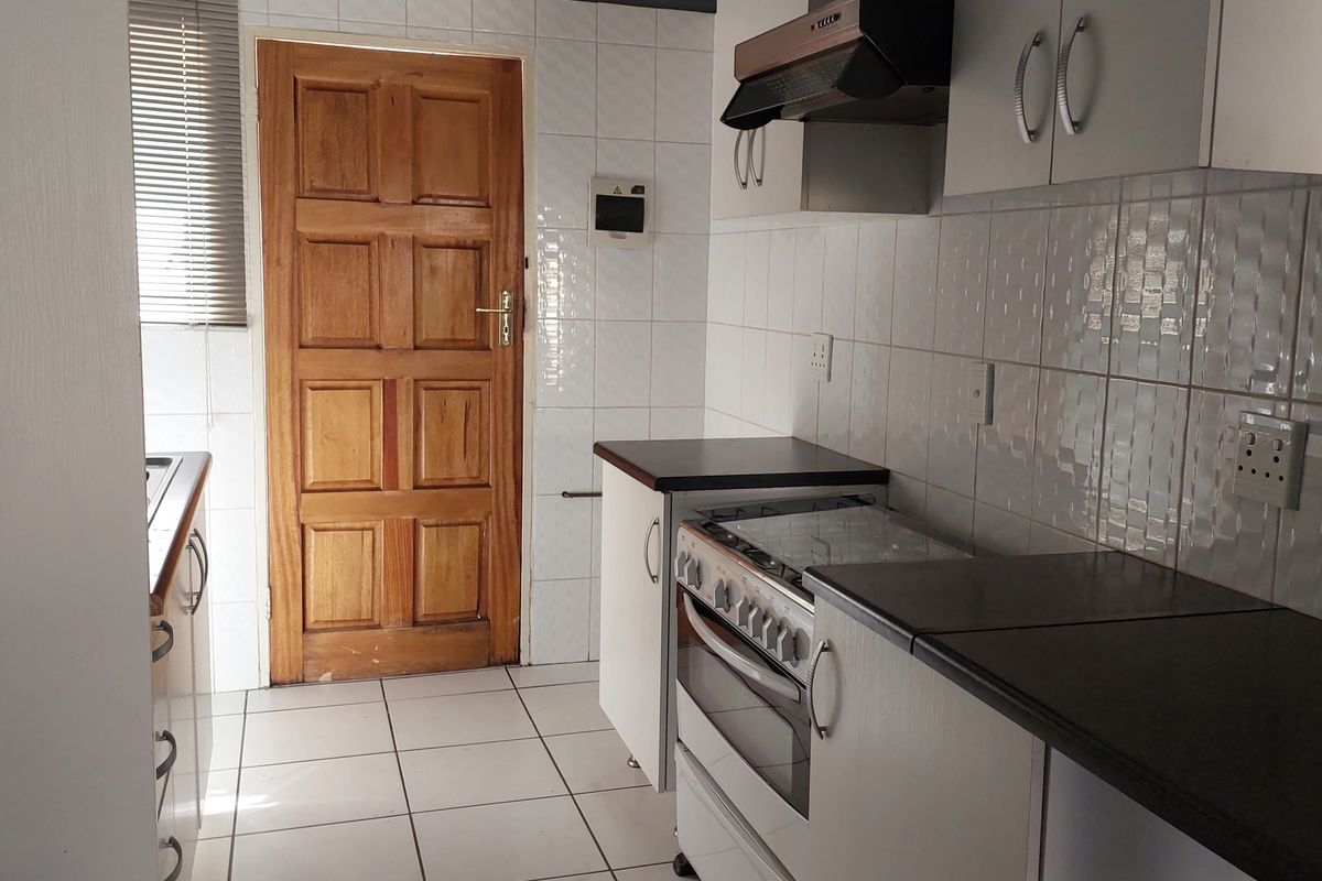 A functional kitchen featuring white cabinetry, tiled backsplash, tiled flooring, and a freestanding stove with an extractor fan.