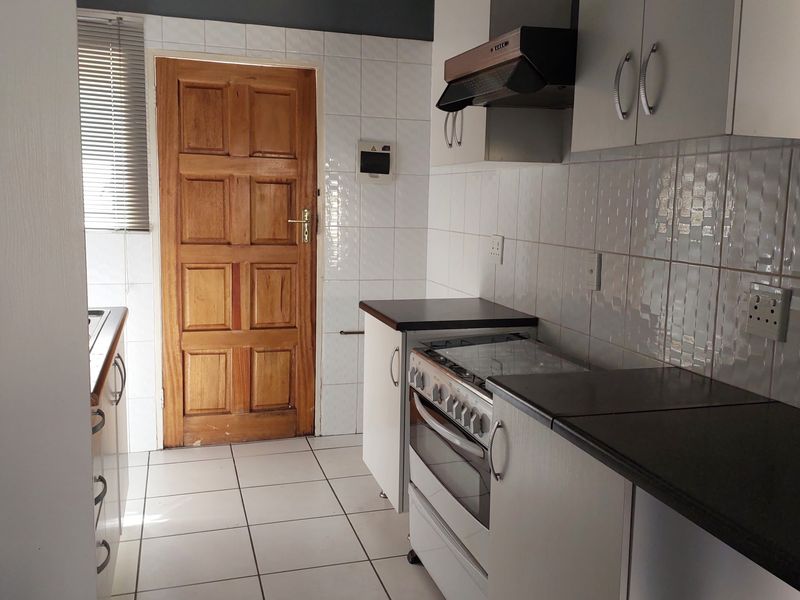 A functional kitchen featuring white cabinetry, tiled backsplash, tiled flooring, and a freestanding stove with an extractor fan.
