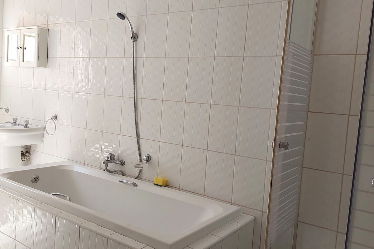 A functional bathroom featuring a built-in bathtub, separate shower enclosure, and pedestal basin with classic white wall tiling.