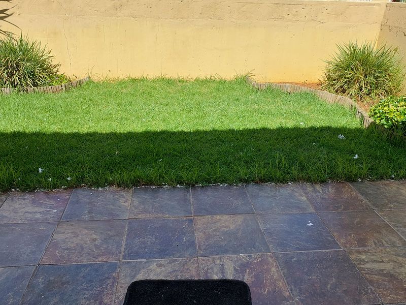 A private rear garden featuring a tiled patio area and a small lawn enclosed by a boundary wall.