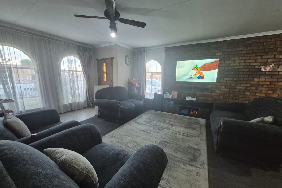 A living room featuring an exposed brick feature wall, arched windows with curtains, and a ceiling fan.