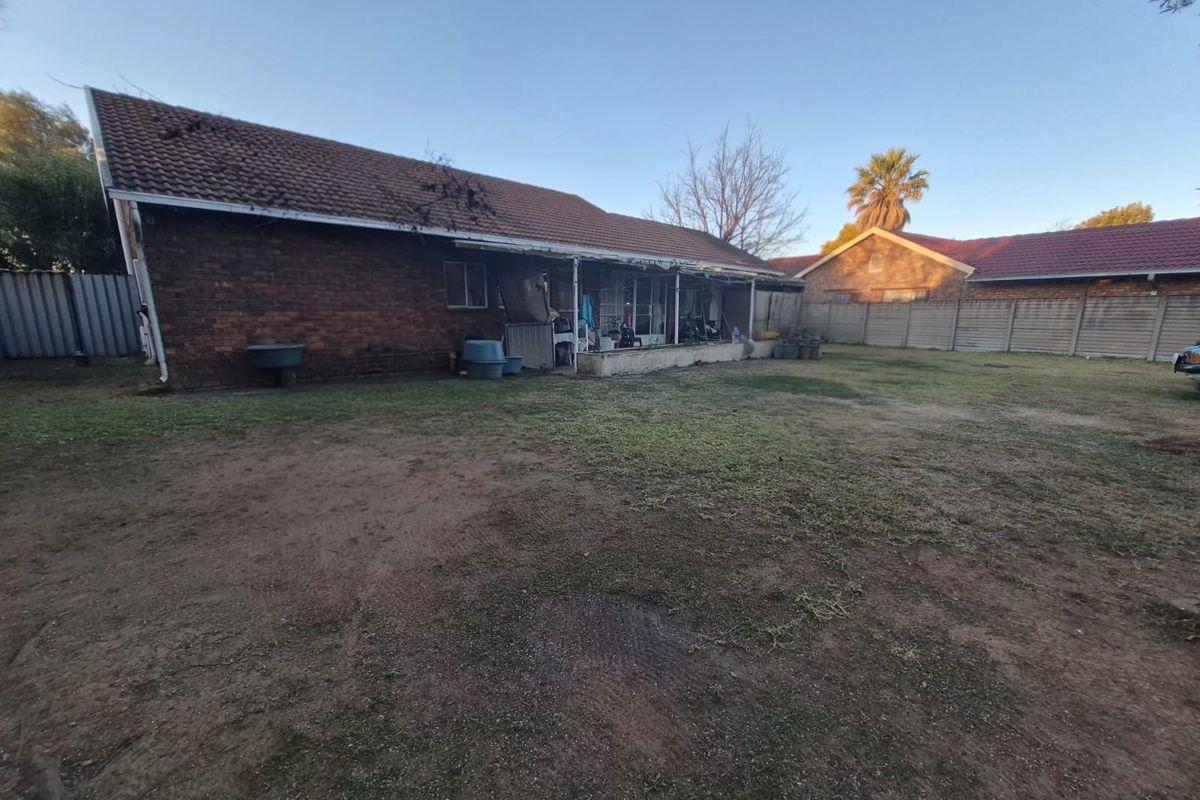Rear view of the property featuring a brick facade, tiled roof, and a covered patio area overlooking a large, unmaintained garden space.