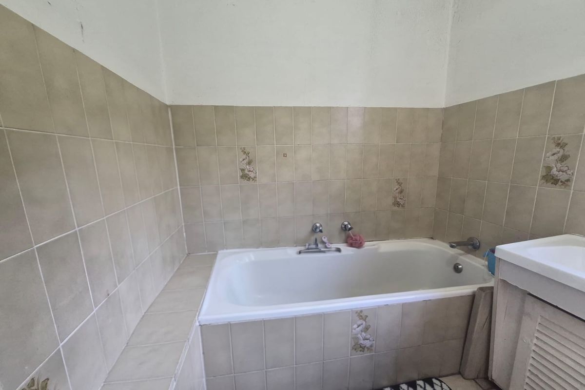 A dated bathroom featuring a built-in bathtub with tiled surround and a vanity unit, requiring cosmetic updates to modernize the space.