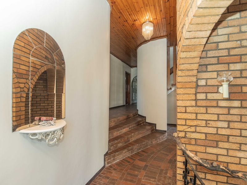 A spacious hallway featuring rustic brick flooring, a distinctive brick archway, and a warm timber-paneled ceiling with a central light fixture.