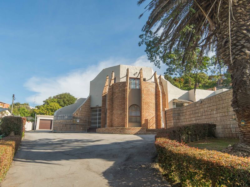 Front elevation of a unique brick-faced house featuring a prominent curved entrance, paved driveway, and secure boundary walling.