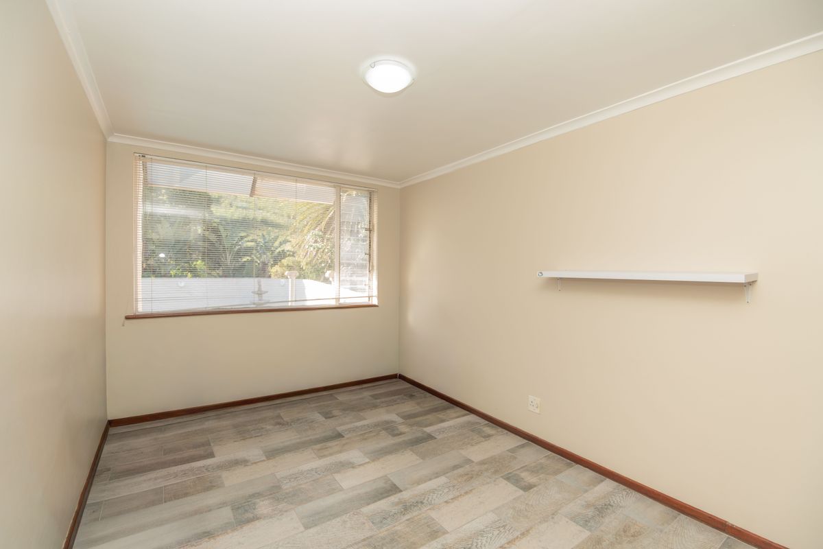 A clean, empty bedroom featuring wood-look tile flooring, neutral walls, and a window with fitted venetian blinds.