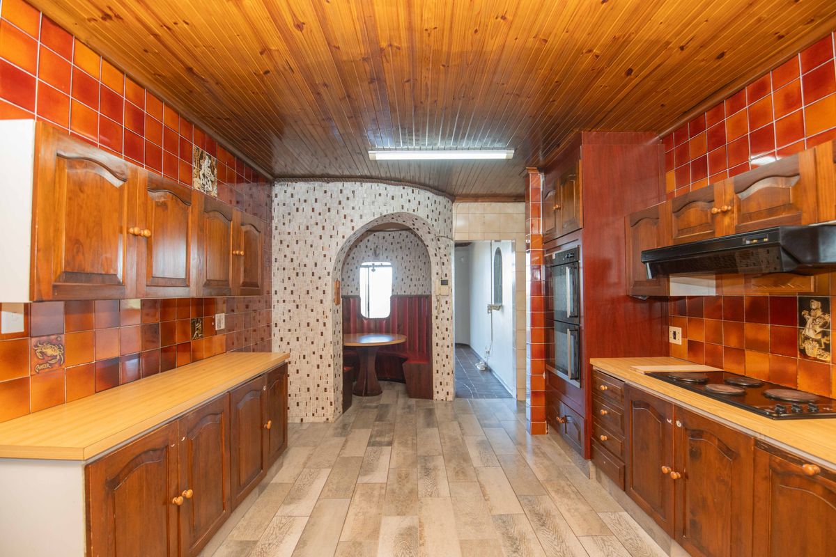 A dated kitchen featuring timber cabinetry, built-in double oven, electric hob, and distinctive tiled walls with a timber tongue and groove ceiling.
