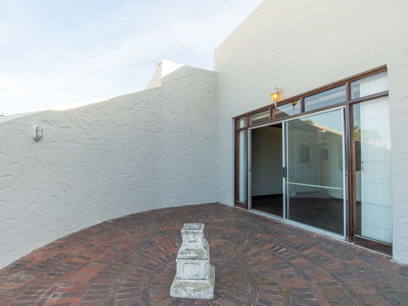 A private outdoor patio area featuring circular brick paving, textured walls, and a large sliding glass door providing access to the interior.
