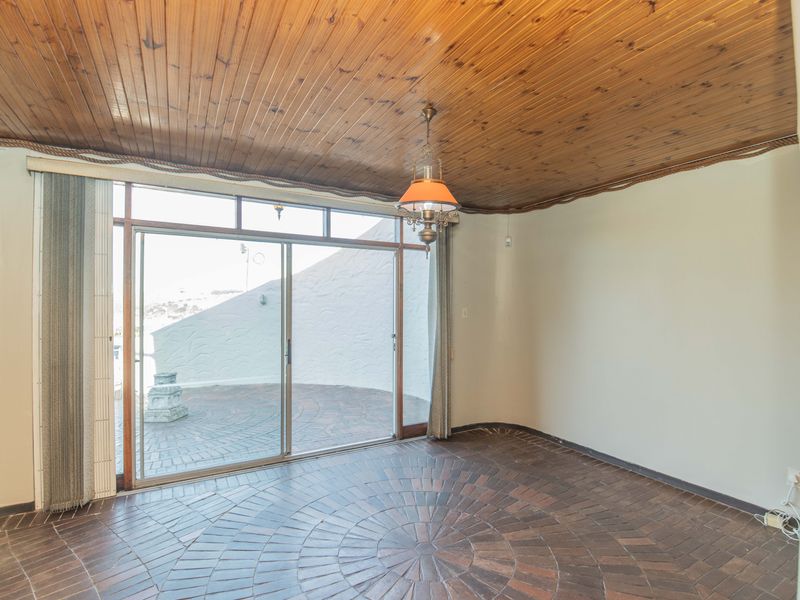 An empty living room featuring a distinctive timber-clad ceiling, circular brick flooring, and a large sliding glass door providing access to an outdoor patio area.