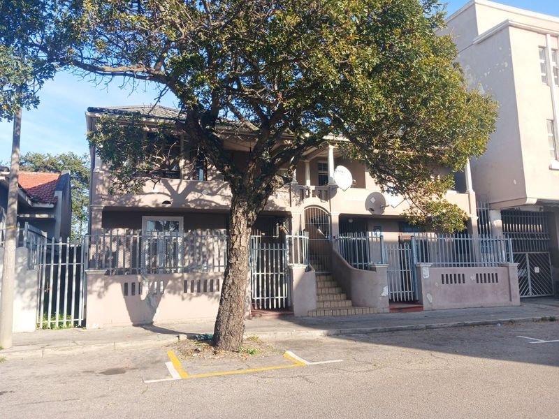 Front elevation of a multi-story apartment building featuring security fencing, a concrete staircase, and a balcony, showing signs of exterior wear.