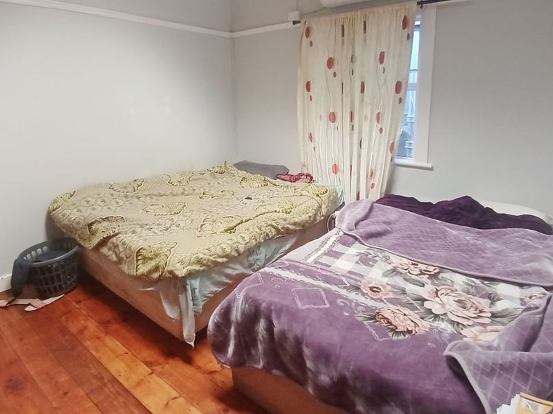 A bedroom featuring timber flooring and a window with curtains.