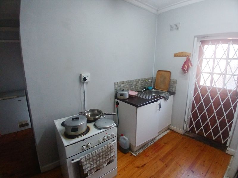Compact kitchen area featuring a sink, tiled splashback, and timber flooring, with direct access to an exterior door protected by a security gate.